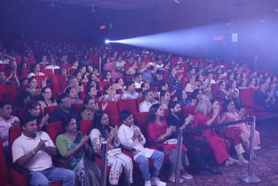 A seated section of the audience clapping as a spotlight beam crosses the hall, children and grandparents in the same rows.
