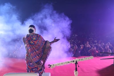 Anshu with an arm outstretched towards the crowd through violet stage smoke, the front row on its feet.