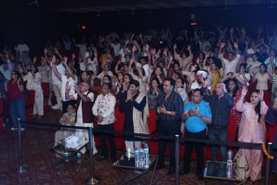 The hall standing with palms together and hands lifted, filling the frame to the back wall.