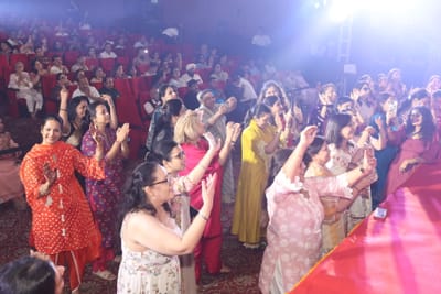 Women standing at the front of the hall, clapping and singing, phones held up to record.