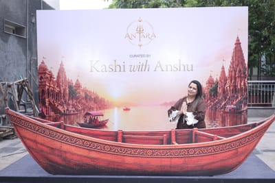 Anshu with hands folded in front of the Kashi with Anshu backdrop and its carved wooden boat.