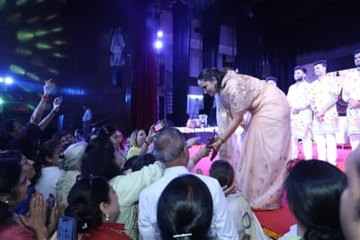 Anshu leaning down from the stage to take the hands of people in the front rows, the band standing behind her.