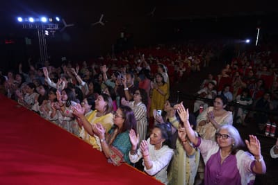 Rows of people at the stage edge with hands raised and clapping, the hall filled behind them.