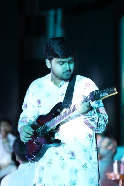 The guitarist mid-phrase with his eyes lowered to the fretboard, lit blue-green against the dark stage.