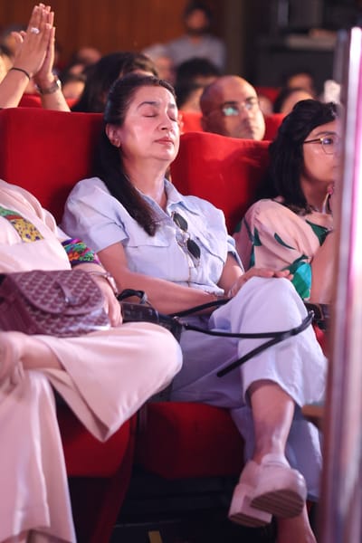 A woman in the audience with her eyes closed and a hand raised, caught mid-bhajan.