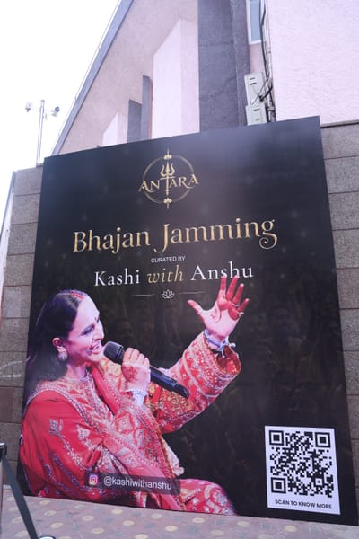 The Antara event banner outside Shah Auditorium, Anshu singing into a microphone with the Kashi with Anshu wordmark and a QR code.