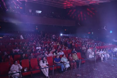 The auditorium seen from the side, seats filled to the balcony under drifting purple light.