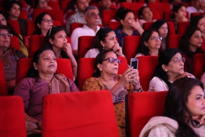Women in the audience watching from the red seats, one holding a phone up to record.