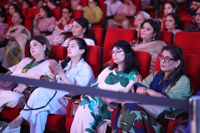 Rows of the audience seated and listening, hands folded in their laps.