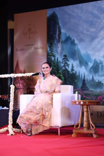 Anshu seated on stage in a pale pink embroidered sari, smiling out at the hall.