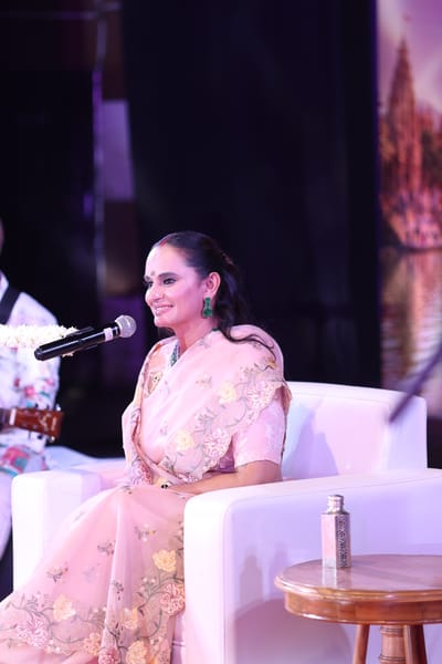 A portrait of Anshu on stage, microphone at her lips, mid-line.