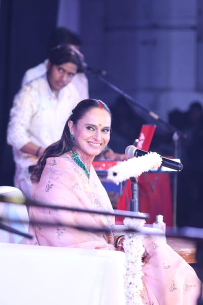 Anshu laughing at the microphone, the keyboard player behind her.