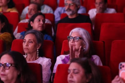 Two older women in the audience, one applauding, watching the stage.