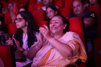 A woman in an orange sari applauding and laughing in the audience.