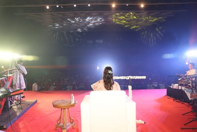 The hall seen from behind Anshu on stage — the keyboard player to one side, the tabla player to the other, the audience beyond the footlights.